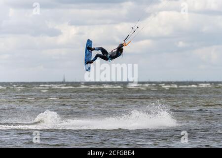 Malmo, Svezia - 23 agosto 2020: Un kitesurfer salta in alto in acqua in una giornata ventosa in cui molte persone cogliano l'opportunità di praticare sport acquatici Foto Stock