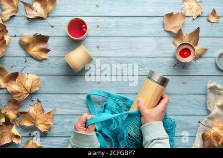 Mani che tengono il sacchetto della rete e il matraccio isolato del thermos di bambù. Zero rifiuti di tè in autunno. Testo A per Autunno. Posa piatta su tavola di legno sbiadita con tazze di bambù un Foto Stock