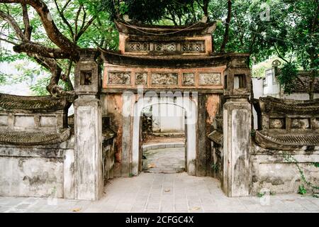 Esterno dell'entrata dell'arco di pietra del vecchio tempio circondato da alti alberi nel cortile Foto Stock