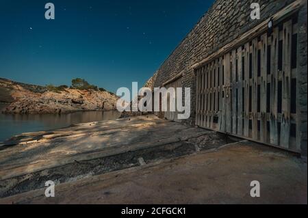 Vecchio edificio in pietra con porte di legno situato contro cielo stellato notte sulla riva di Cala es Canaret, Ibiza, Spagna Foto Stock