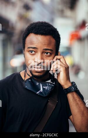 Uomo nero che parla sul cellulare con espressione seria nel via Foto Stock
