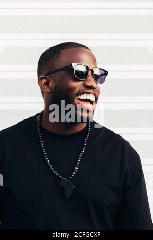 Felice uomo nero che posa e sorride su sfondo bianco e. indossare occhiali da sole neri Foto Stock