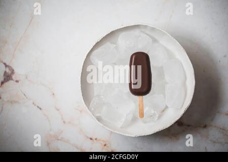 Vista dall'alto del gelato al cioccolato in una ciotola con cubetti di ghiaccio posti su una superficie di marmo Foto Stock