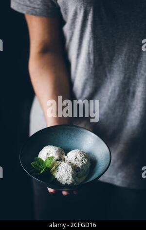 Vista di raccolto di anonima Donna che tiene ciotola con stracciatella gelato palline decorate con foglie di menta Foto Stock