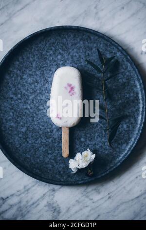 Vista dall'alto, ancora in vita, di un papsiclo cremoso di lamponi piatto scuro sulla superficie di marmo e decorato con fiori Foto Stock