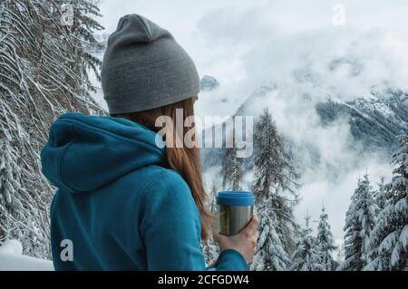 Giovane ragazza con una tazza termica che si affaccia sui monti Dolomiti il giorno fresco nuvoloso Foto Stock