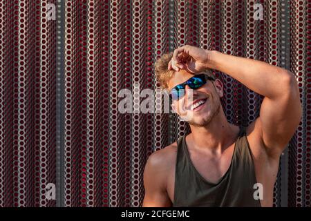Bel giovane ragazzo sorridente e guardando la macchina fotografica mentre si è in piedi vicino al muro di metallo sulla strada della città Foto Stock