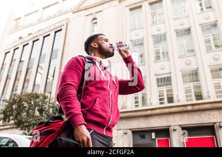 Giovane uomo sportivo che beve acqua per strada Foto Stock