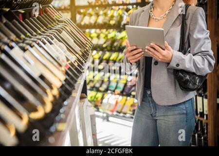 Donna d'affari senza volto in giacca grigia che tiene e naviga tablet in piedi con un amico. Foto Stock
