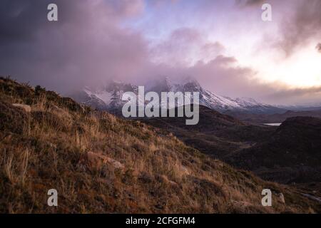 Paesaggio pittoresco di altopiano selvaggio con cime innevate e. creste tra le nuvole drammatiche durante il tramonto Foto Stock