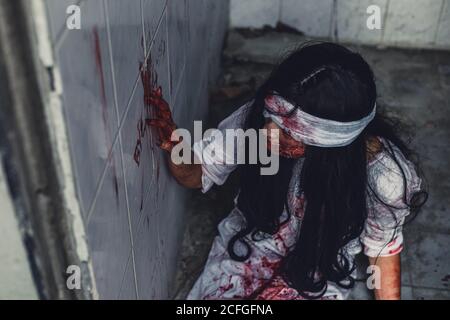 Halloween ragazza che scrive la parola 'Bye' sul muro. Le donne fantasma indossano un abito bianco macchiano sangue in casa abbandonata. Concetto di Halloween Foto Stock