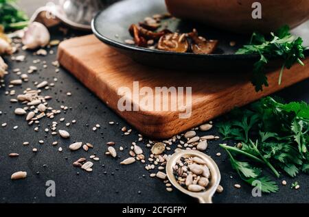 Vari semi ed erbe hanno versato intorno al tagliere di legno e. ciotola con funghi secchi durante la preparazione del cibo in cucina Foto Stock