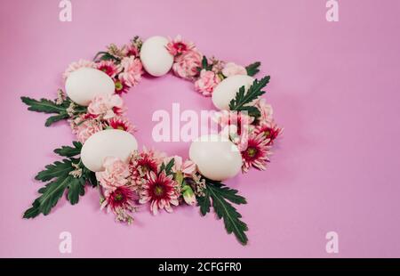 Dall'alto elegante corona pasquale fatta di fiori e pollo uova e posto su sfondo rosa Foto Stock