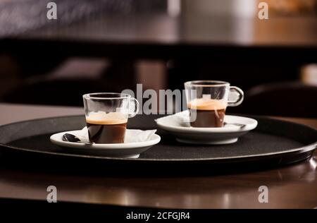 Due tazze di caffè caldo appena preparato, sul vassoio del cameriere, sul tavolo di legno, all'interno della caffetteria e spazio libero per la decorazione. Foto Stock