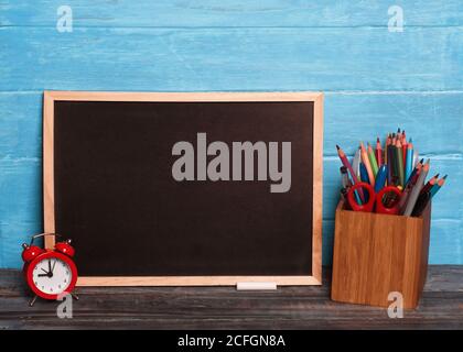 Mockup di bordo nero, matite, mantello, gessetti su sfondo di legno Foto Stock