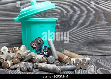 Batterie usate corrose. Nelle vicinanze c'è un cestino. Su tavole di pino. Smaltimento di rifiuti pericolosi. Foto Stock