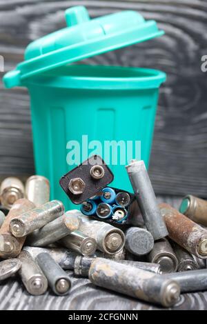 Batterie usate corrose. Nelle vicinanze c'è un cestino. Su tavole di pino. Smaltimento di rifiuti pericolosi. Foto Stock
