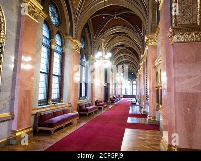 Sala sontuosa ma vuota del Parlamento ungherese: Un lungo corridoio fiancheggiato da finestre, illuminato da lampadari e arredato con una moquette rossa e lunghi divani all'esterno delle sale riunioni nelle palazzine del parlamento. Foto Stock