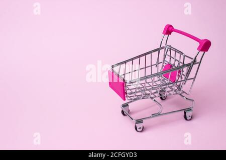 Mini shopping cart tema retail cart poco su un sfondo di carta rosa Foto Stock