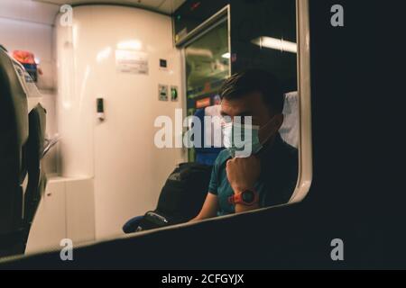 L'uomo caucasico guarda fuori la finestra di un treno notturno con uno sguardo triste in una maschera medica per proteggere contro l'epidemia di coronavirus. Sicurezza in pubblico Foto Stock