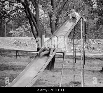 ANNI '70 SORELLA BAMBINA CHE SALE FINO ALLA CIMA E RAGAZZO FRATELLO CHE SCENDE PRIMA LA TESTA SU UN ALTO BORDO SCORREVOLE NEL PARCO GIOCHI - J13145 HAR001 HARS FEAR FUMETTO SLIDE GIOIA STILE DI VITA FEMMINE FRATELLI HOME VITA COPIA SPAZIO A LUNGHEZZA PIENA PERICOLO MASCHI RISCHIO DI FRATELLI SUBACQUEI SORELLE B&W DIVERTENTE AVVENTURA SCOPERTA TEMPO LIBERO ED ECCITAMENTO RICREAZIONE CHE SCIVOLA COMICO DENTRO SOPRA A FRATELLO CONCETTUALE DAREDEVIL COMMEDIA TESTA PRIMI GIOVANI TOGETHERNESS BIANCO E NERO ETNIA CAUCASICA HAR001 VECCHIO STILE Foto Stock