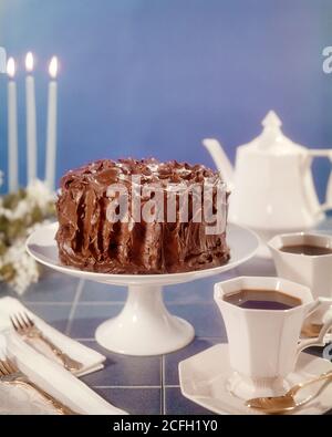 TORTA GHIACCIATA AL CIOCCOLATO DEGLI ANNI '70 SU UNA CAFFETTIERA A FORMA DI TORTA BIANCA TAZZE E PIATTINI FORCHETTE TOVAGLIOLI TRE CANDELE BLU - KF8548 PIANO PORTAPAZIENTE HARS PHT001 Foto Stock