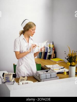 1960S 1970 DONNA INFERMIERE ASSISTENZA RICETTISTA IN CAP E. STUDIO MEDICO UNIFORME DI PICCOLE DIMENSIONI CHE REGISTRA LE INFORMAZIONI DEL PAZIENTE - KM5762 PHT001 HARS SIGNORE PERSONE PROFESSIONE DI CURA ABILITÀ DI PROFESSIONE DI SALUTE ABILITÀ DI OCCUPAZIONE DI BENESSERE PROVIDER DI SERVIZI PROFESSIONISTI HEALING CARRIERE CONOSCENZA LAVORO SALUTE LAVORO ASSISTENZA OCCUPAZIONE PROFESSIONI GUARITORE CONCETTUALE EFFICIENTE PROFESSIONISTA ELEGANTE DIPENDENTE PROFESSIONISTI GIOVANI ADULTI DONNA CAPACE ETNIA CAUCASICA LAVORARE VECCHIO STILE Foto Stock