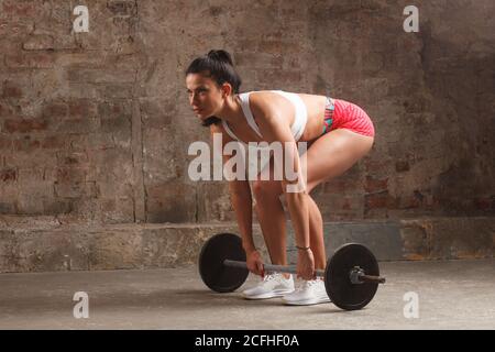 donna in forma attraente che fa l'esercitazione di deadlift in interno brutale della palestra Foto Stock