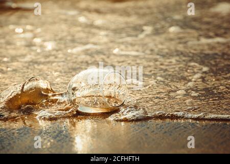 bicchiere di vino in spiaggia e acqua di mare in ingresso ora d'oro Foto Stock