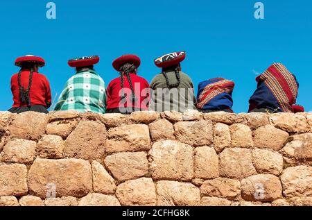 Popolo peruviano indigeno Quechua seduto su un muro Inca, Chinchero, Provincia di Cusco, Perù. Foto Stock