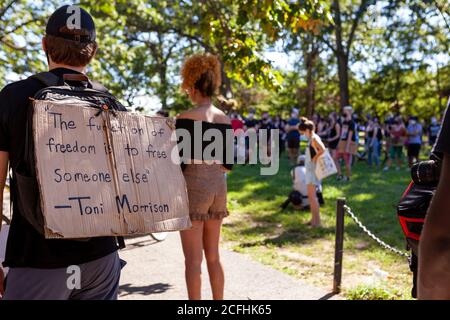 Washington, DC, USA, 5 settembre 2020. Nella foto: Un uomo indossa un cartello sulla schiena che dice: 'La funzione della libertà è quella di liberare qualcun altro - toni Morrison,' mentre attende la marcia della giustizia per l'inizio di Deon Kay. Una grande folla è visibile in lontananza, e questa folla cresce ogni settimana mentre continuano le molestie e le aggressioni contro i manifestanti da parte della polizia metropolitana (DC). Deon Kay era un adolescente ucciso dalla polizia metropolitana all'inizio della settimana. L'uccisione è controversa perché la polizia ha rilasciato resoconti contraddittori dell'uccisione. Credito: Allison C Bailey/Alamy Foto Stock