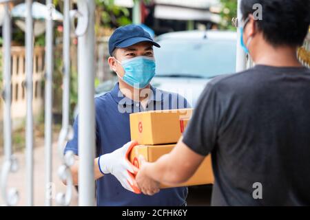 Consegna uomo asiatico che tiene scatole di cartone in guanti di gomma medica e maschera. Shopping online e consegna espressa o ecommerce. Concetto prevenire il s Foto Stock