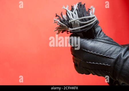 La mano maschile in guanto di pelle regge la sciarpa di lana grigia. L'uomo sta mostrando la sua mano in guanto nero di pelle su sfondo corallino. Vista laterale. Messa a fuoco selettiva. Foto Stock