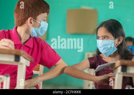 Due bambini in maschera medica in classe si salutano l'un l'altro con i colpi di gomito, mantenendo la distanza socail a scuola - concetto di scuola riapre, indietro Foto Stock