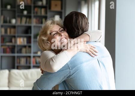 Primo piano sorridente donna matura con occhiali che abbracciano figlio adulto Foto Stock