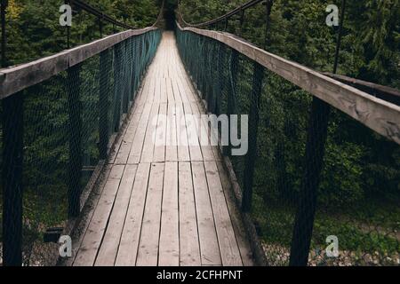 Vista panoramica del ponte sospeso in acciaio lungo. Vecchio piccolo ponte di legno sul fiume solo per pedoni. Fiume di montagna circondato da montagne e. Foto Stock