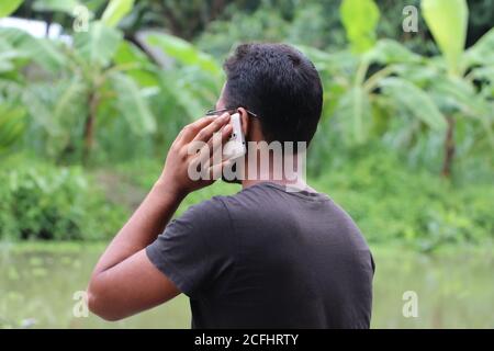 Vista posteriore laterale di un giovane uomo d'affari che parla sul telefono cellulare. Parlare di nuovo progetto. Lavorare al di fuori del concetto Foto Stock