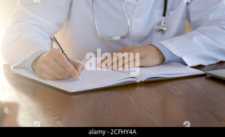 Primo piano medico che scrive nella scheda paziente, lavorando con i documenti Foto Stock