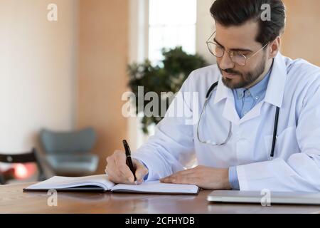 Serio medico sicuro che scrive nei documenti, lavorando in ufficio Foto Stock