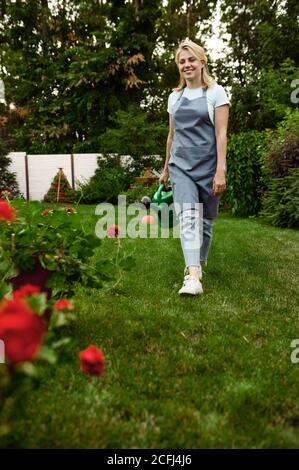 Donna in grembiule tiene annaffiatura lattina in giardino Foto Stock