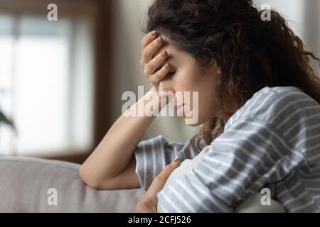 La donna che si siede sui copriletto del divano con la palma si sente turbata Foto Stock