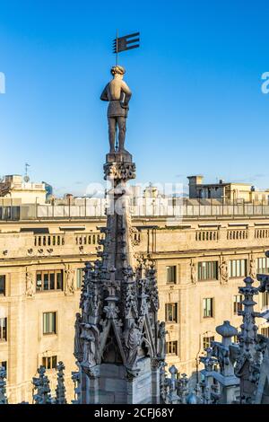 Milano, Italia - 23 dicembre 2019 - la statua di Male si erge sulla sommità di una torre del Duomo, la famosa chiesa di Milano, in Italia, su una chiara e luminosa facciata blu Foto Stock
