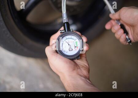 Uomo che controlla manualmente la pressione dell'aria della ruota del motociclo prima di procedere Foto Stock