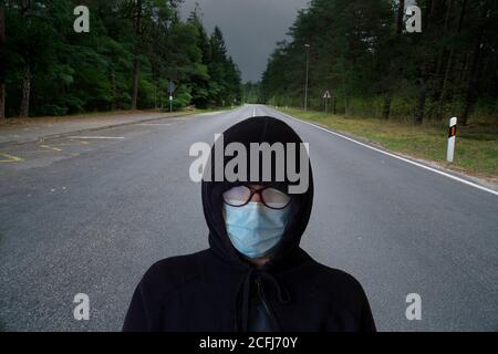 Una donna con una maschera protettiva è in piedi in mezzo alla strada. Concetto di una lunga strada per il recupero. Foto Stock