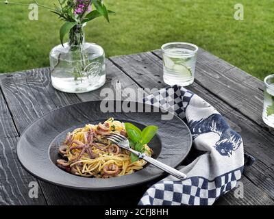 Spaghetti con calamari. Pasta di pesce con basilico verde in piatto nero su tavola rustica. Foto Stock