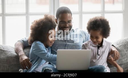 Felice padre afroamericano che usa il computer con i bambini. Foto Stock
