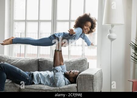 Giovane etnia africana papà sollevando le mani felice figlia. Foto Stock