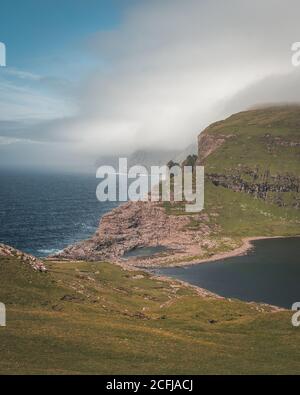 Faroe Islands Traelanipa la scogliera di roccia degli schiavi si vede innalzarsi sopra l'oceano vicino al lago Sorvagsvatn. Nuvole e cielo blu durante suommer sul Foto Stock