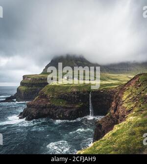 Gasadalur villaggio e Mulafossur la sua cascata iconica, Vagar, Isole Faroe, Danimarca. Vista approssimativa nell'oceano atlantico settentrionale. Verdi lussureggianti durante l'estate Foto Stock