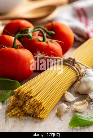 Spaghetti crudi legati in un fascio con pomodori freschi di vite, aglio e basilico su un rustico tavolo di legno Foto Stock